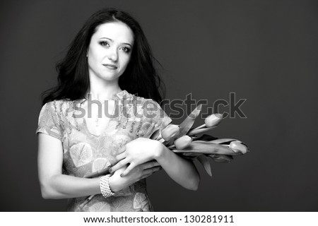 Black and white image of a beautiful young woman with long healthy hair in a beautiful dress holding a bouquet of tulips