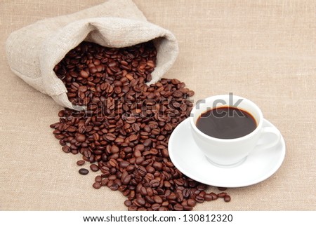White cup with black coffee, with lots of coffee beans around it