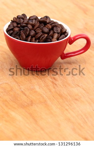 Red coffee cup full of coffee beans on a light wooden background on Food and Drink