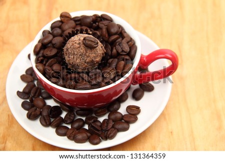 Red coffee cup with heart symbol full of raw coffee beans and chocolate on old wooden plank