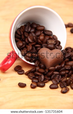 Red cup with coffee beans and chocolate heart symbol on wooden background on Food and Drink theme