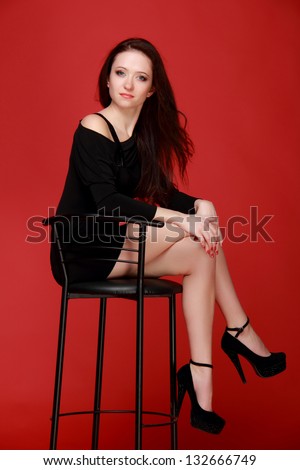 Pretty nice woman with dark hair sitting in a high chair with a red background on Beauty and Fashion