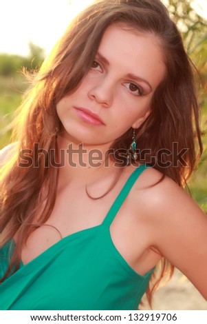 Charming sad young woman with dark long hair in a summer dress in the park