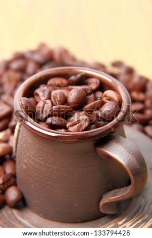 Brown coffee beans in small ceramic coffee cup over light brown wooden background on Food and Drink