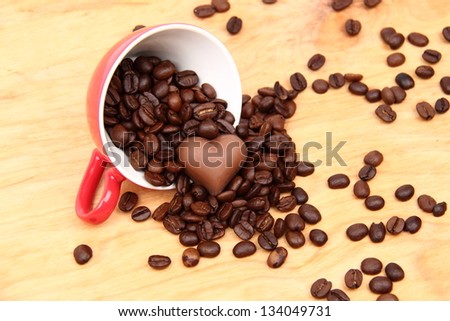 Red cup with coffee beans and sweets in the form of heart on  wooden background on Food and Drink