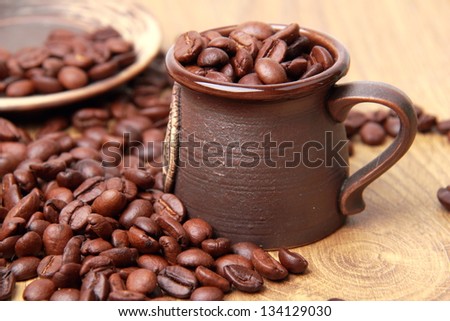 Lots of coffee beans in small ceramic coffee cup over light brown wooden background