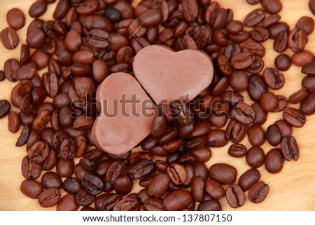 Chocolates in the form of heart with lots of coffee beans over light brown wooden background