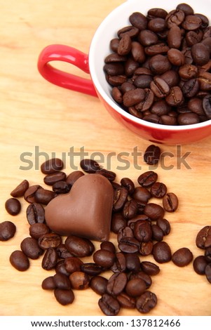 aroma coffee beans in red ceramic coffee cup with heart symbol and yummy chocolate heart on wooden desk