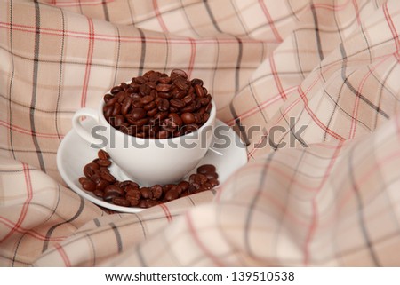 White cup full of coffee beans on a beige fabric on Food and Drink