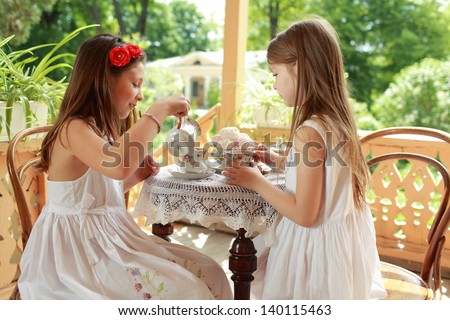 Caucasian beautiful young girls sitting at a table drinking tea and eat marshmallows outdoors