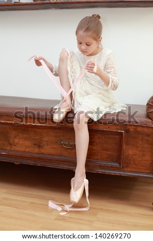 Beautiful young ballet dancer in a white dress sits on a chair and puts on pointe