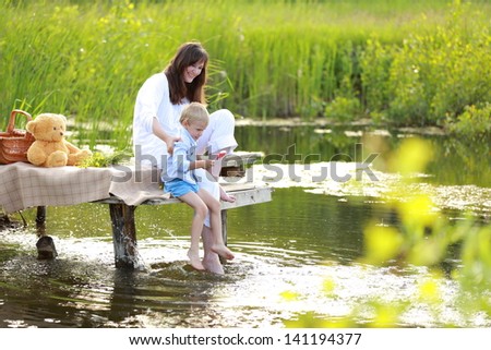 Beautiful mother with a young son sitting by the lake with her Ã?Â¢??Ã?Â¢??bare feet in the summer