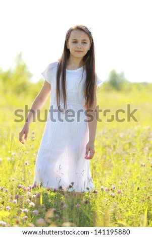 Smiling cute little girl in a white dress running across the field with wild flowers in the sun