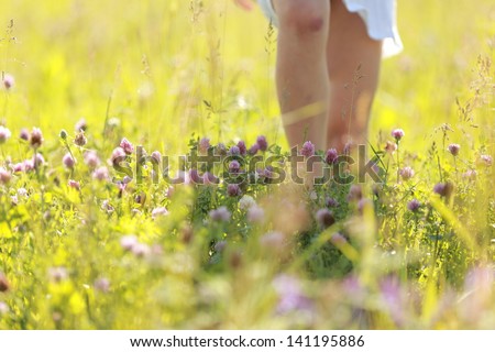 little girl in a white dress running across the field with wild flowers in the sun