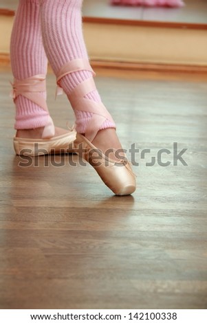 Legs a little ballerina in a pink ballet shoes and socks in ballet poses trains in ballet hall on the floor