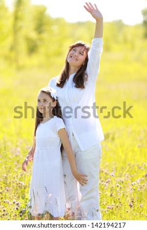 Beautiful mother and daughter with long dark hair walking and laughing in a green park at sunset