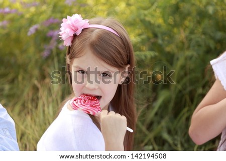 Cheerful young children eat more candy on a stick on a background of green grass outdoors