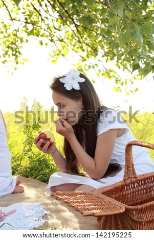 Beautiful young girl in a white dress with a sweet smile sitting on a picnic outdoors