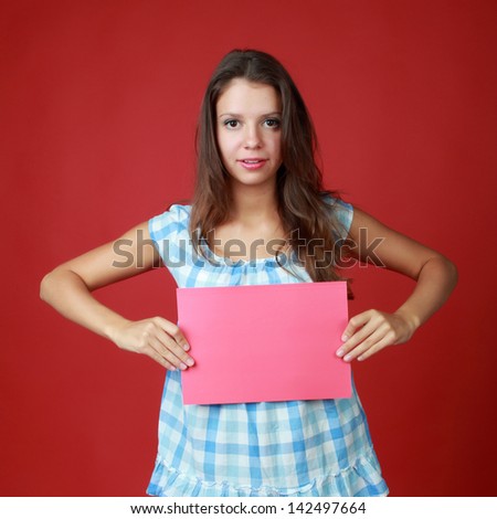 Studio portrait of a happy girl with a pink sheet of paper for text on a red background