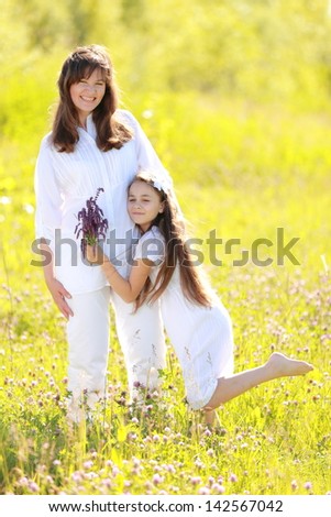 Smiling and cheerful mother and daughter with long dark hair walking and laughing at summer green grass outdoors