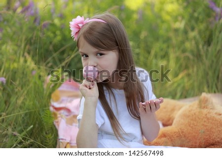 Little girl is drinking imaginary tea from a toy cup on the background of tall green grass with wildflowers