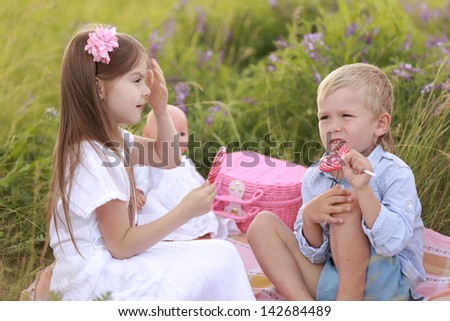 Smiling young children sitting in the green grass with wildflowers and a large eat lollipops