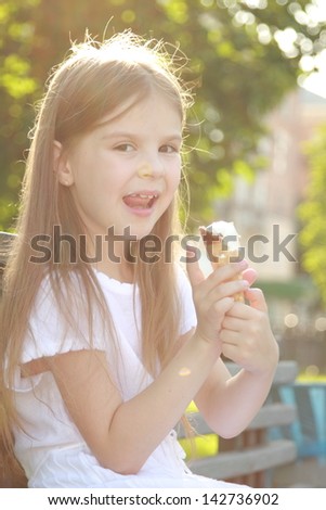 Little girl in a white dress is white ice cream outdoors