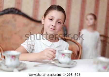 Cute little girls sitting at the dinner table and drink tea from classic ceramic cups