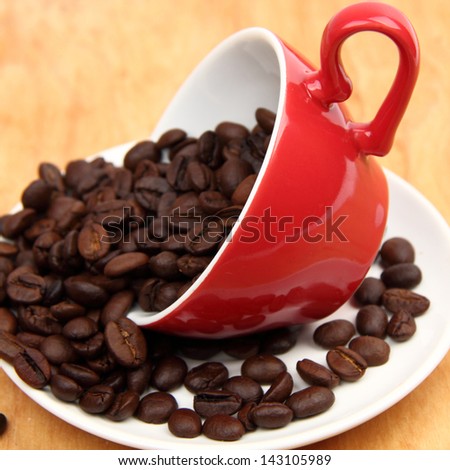 Arabic coffee beans in red ceramic coffee cup over wooden desk