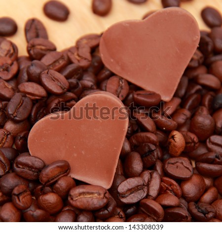 Chocolates in the form of heart with lots of coffee beans over light brown wooden background/Delicious chocolate heart symbol candies and dark brown coffee beans
