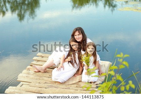 Charming woman and two young children rest on the nature of the serene backdrop of the pond