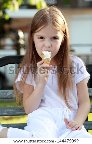 Little girl in a white dress is white ice cream outdoors