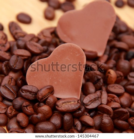 Chocolates in the form of heart with lots of coffee beans over light brown wooden background/delicious chocolate heart symbol candies and dark brown coffee beans