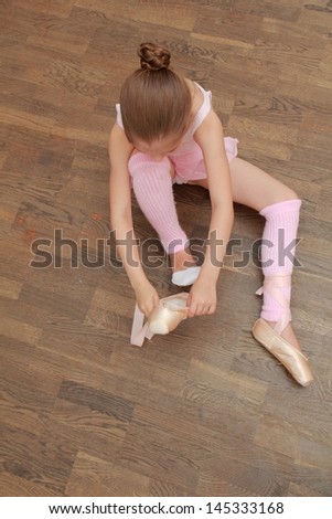 Charming ballerina puts on pointes in a pack sitting on the old wooden floor in the ballet hall