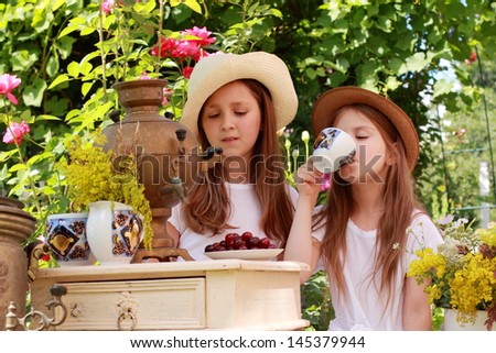 Children drink tea from an old Russian samovar in the garden in the street / Russian national traditions
