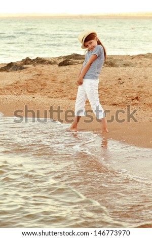 smiling little girl on the beach wets feet in water at sunset on the outdoor