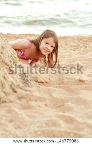 Beautiful smiling little girl in a pink swimsuit is played in the sand on the beach