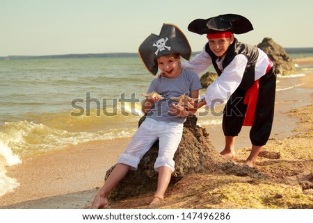 Beautiful little boy and girl dressed in pirate costumes and holding starfish on the beach