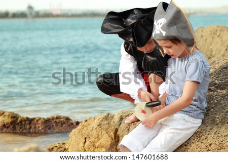 Cute little girl and boy in beautiful costumes, pirate hats and looking for treasure in the seaside