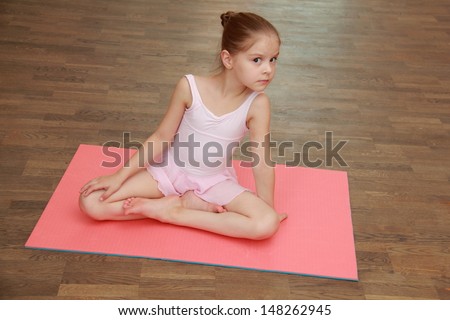 Little gymnast in a suit for the gym warming up on the wooden floor in the ballet hall