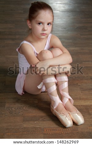 Sad little ballerina sitting on an old wooden floor wearing ballet shoes