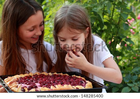 Charming smiling little girls eat homemade cherry pie and laughing in the summer garden