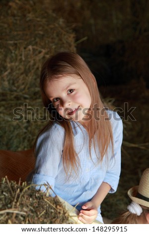 Beautiful little girl in a hat sitting on the hayloft with a book to read and play