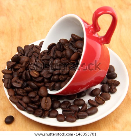 arabic coffee beans in red ceramic coffee cup over wooden desk