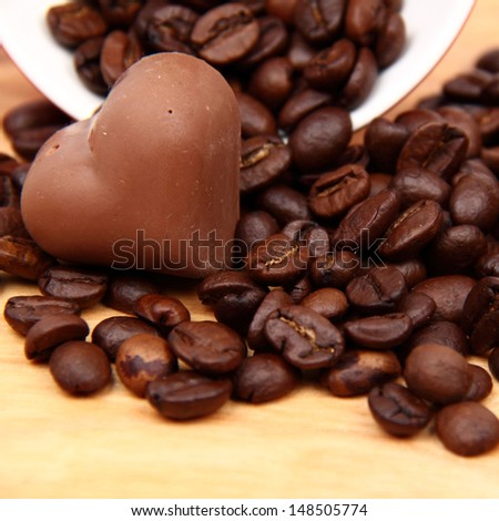 Coffee beans in red ceramic coffee cup with heart symbol and yummy chocolate heart on wooden desk