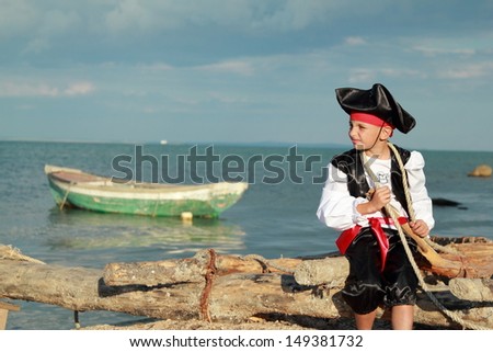 Small Somali pirate on a background of blue sea with a boat/Handsome Boy dressed as a pirate on the sea coast