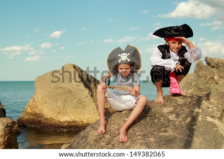 boy and girl in a pirate costume and a beautiful pirate hats sitting on a large rock at the seaside/Fancy Dress Pirates