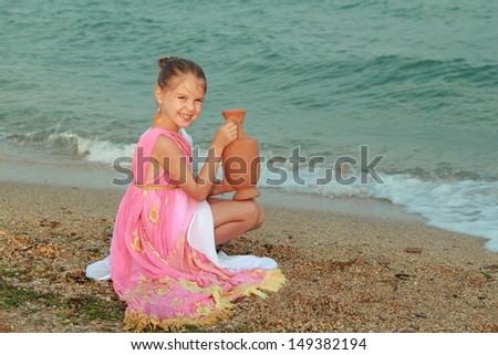 girl in a beautiful dress in Greek style with an amphora stands barefoot in the sea water at the seaside