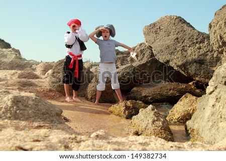 boy and girl in a pirate costume with a map and a magnifying glass looking for buried treasure on the beach