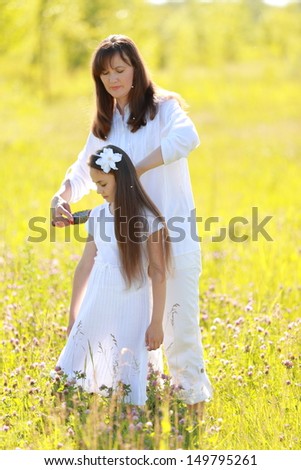 Beautiful mother and daughter with long dark hair walking and laughing in a green park at sunset